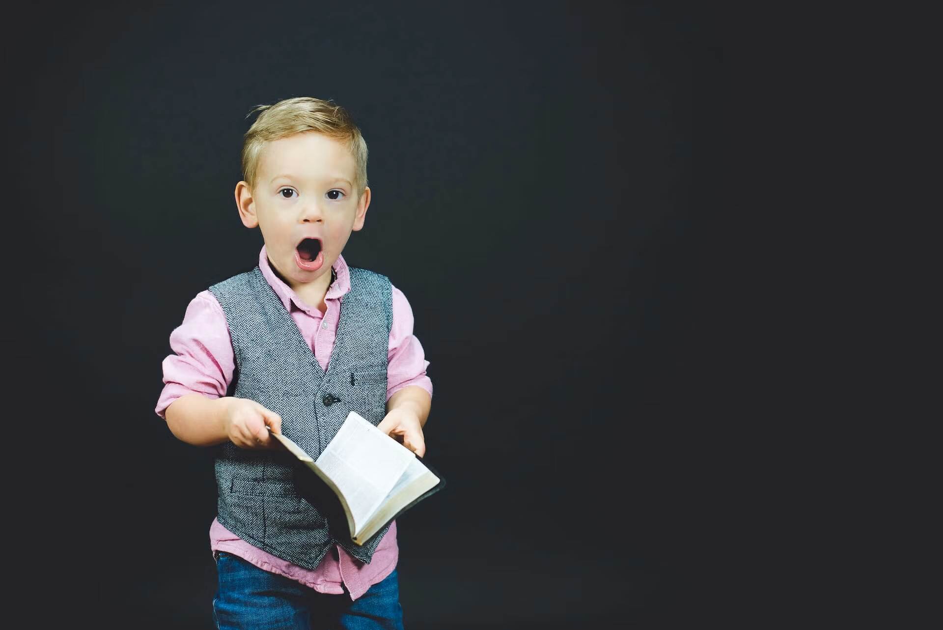 Un jeune garçon affiche un visage surpris, avec un livre à la main