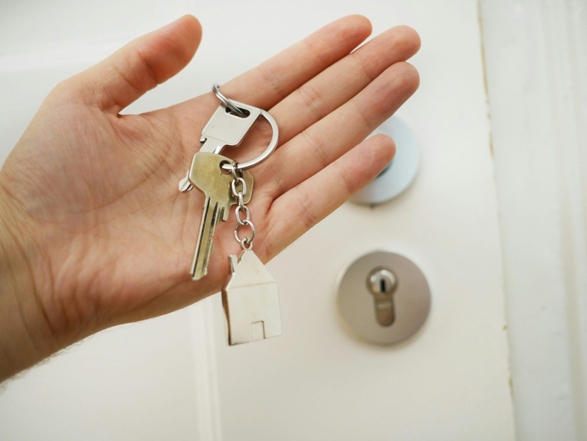 Une main tient les clefs d'une maison devant une porte d'entrée