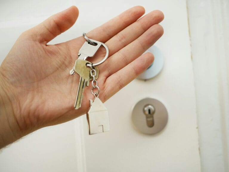 Une main tient les clefs d'une maison devant une porte d'entrée