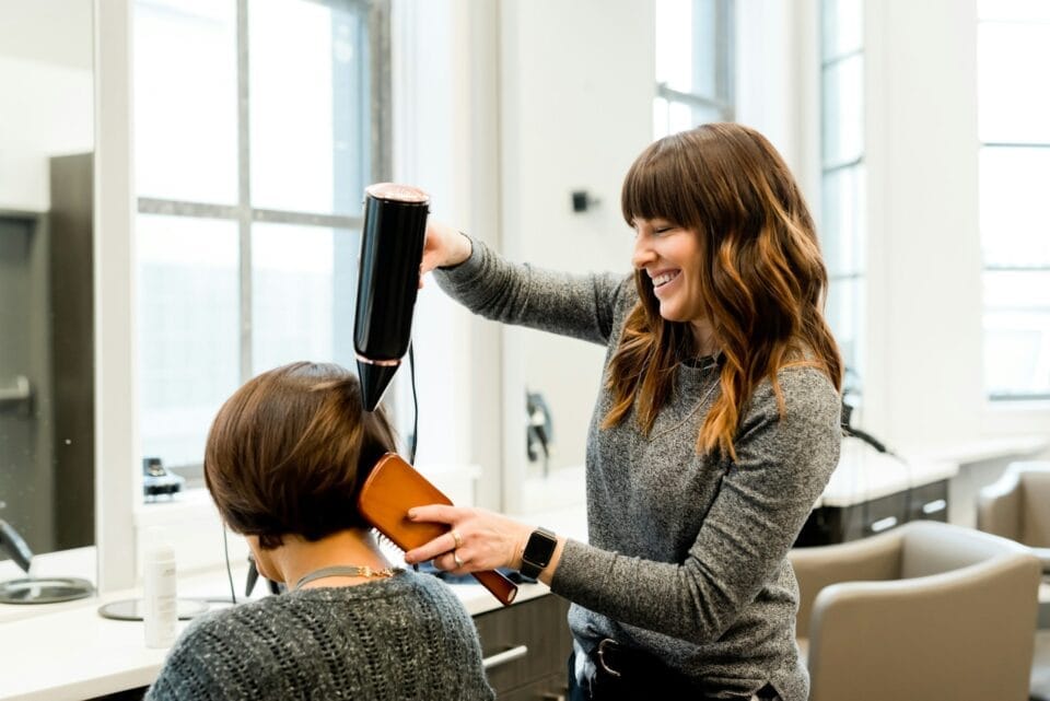 Coiffeuse souriante utilisant un sèche-cheveux