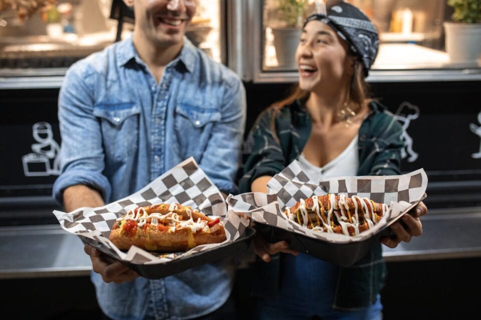 Couple souriant tenant des hot-dogs garnis