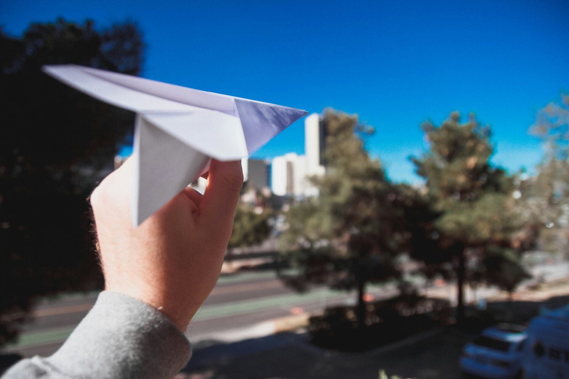 Une main sur le point de lancer un avion en papier dans la rue.