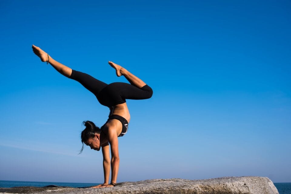 Woman performing advanced yoga pose on seaside rock