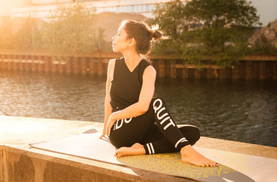 Woman meditating by river at sunset