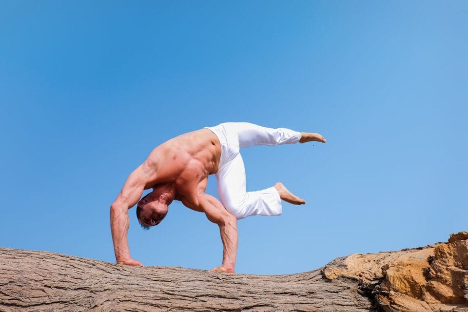 Man performing advanced yoga pose outdoors on rock